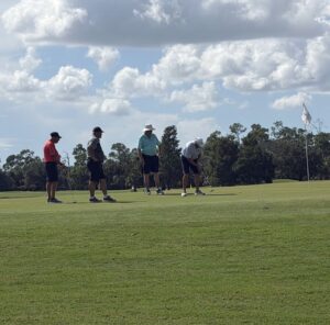 Four golfers putting on the green at the Drive Out Hunger tournament