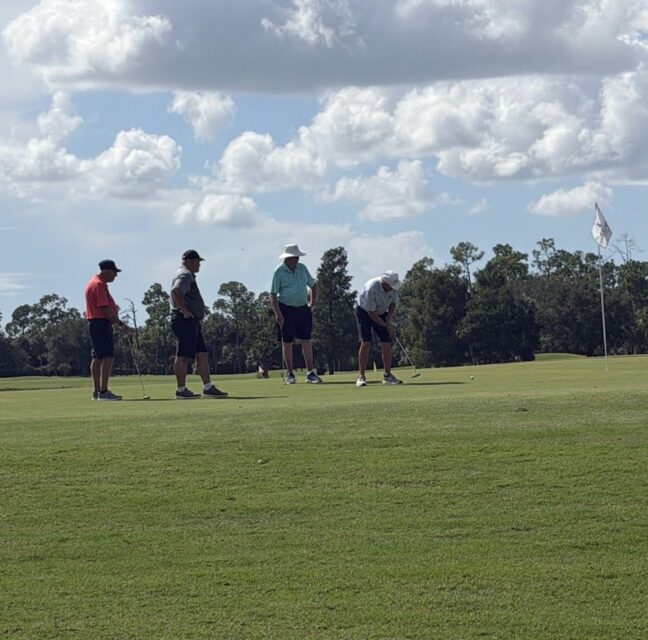 Four golfers putting on the green at the Drive Out Hunger tournament