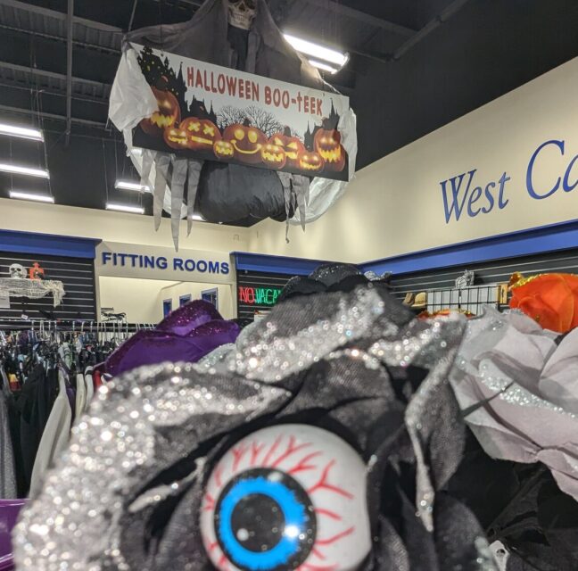 Halloween Boo-teek banner above costume racks and eyeball masks at Goodwill