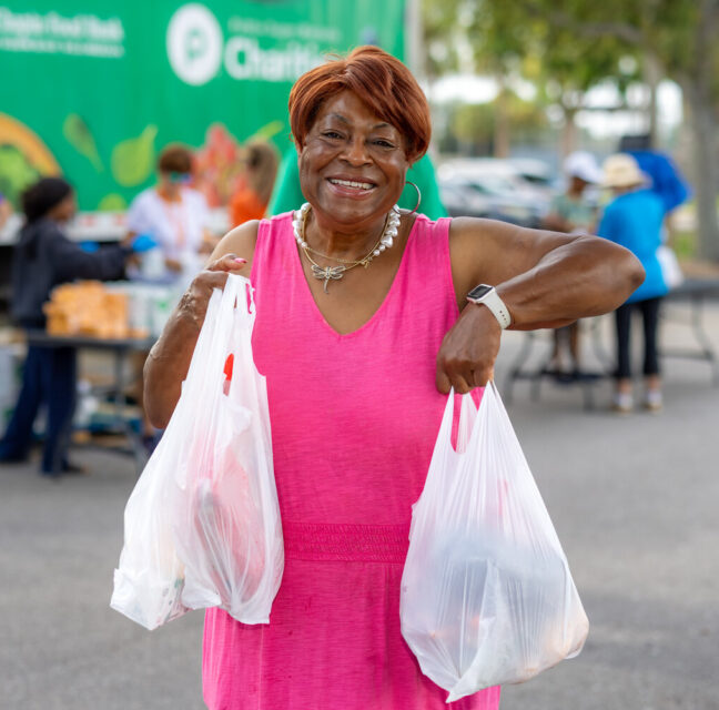 Mary Brown smiling as she carries two bags of groceries from a Harry Chapin Food Bank distribution