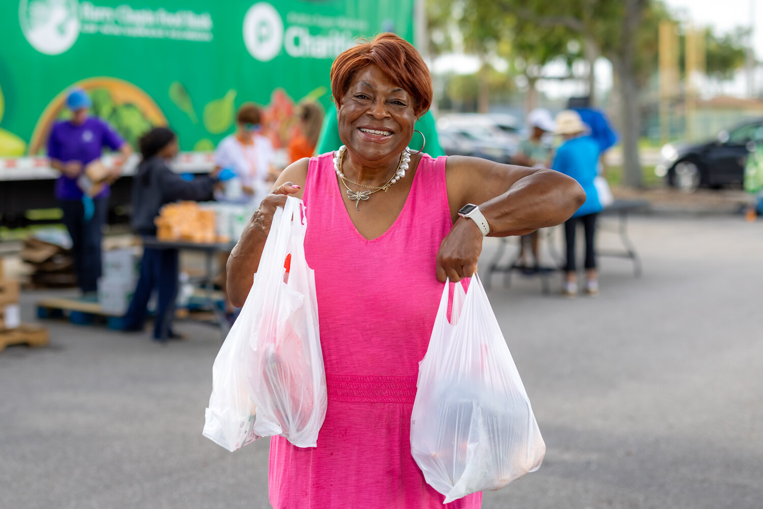 Mary Brown smiling as she carries two bags of groceries from a Harry Chapin Food Bank distribution