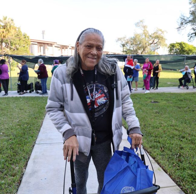 Smiling woman with a walker and tote bag at a Farm Share food distribution