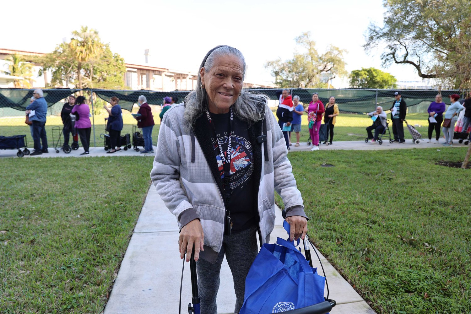 Smiling woman with a walker and tote bag at a Farm Share food distribution
