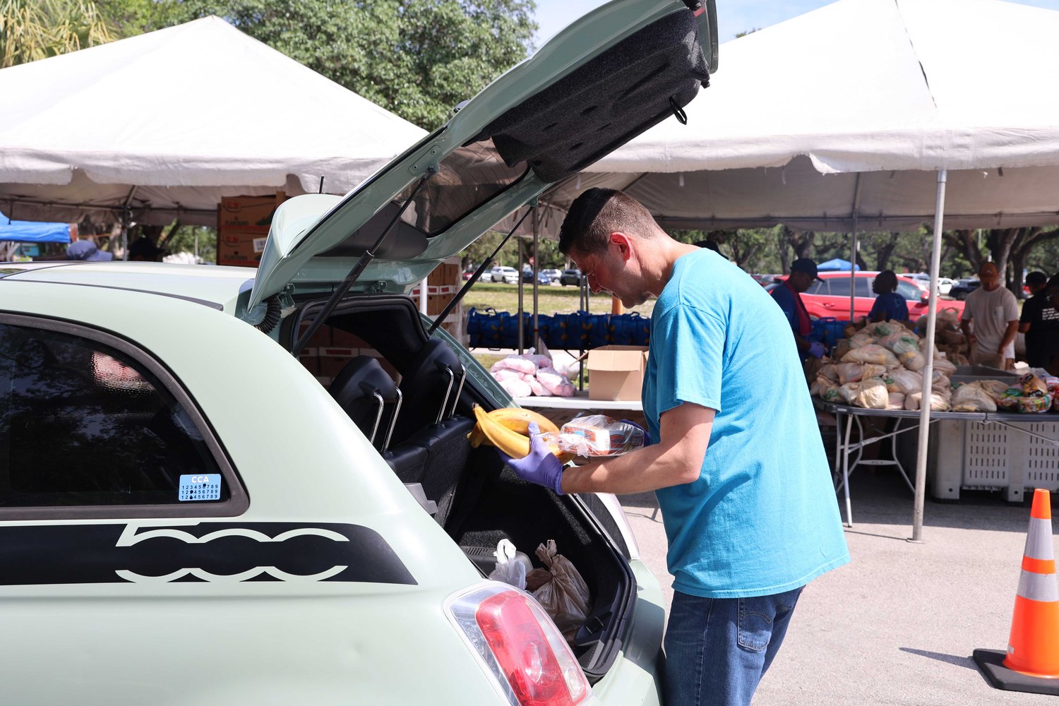 Volunteer loading bananas and bread into a car trunk at a food distribution