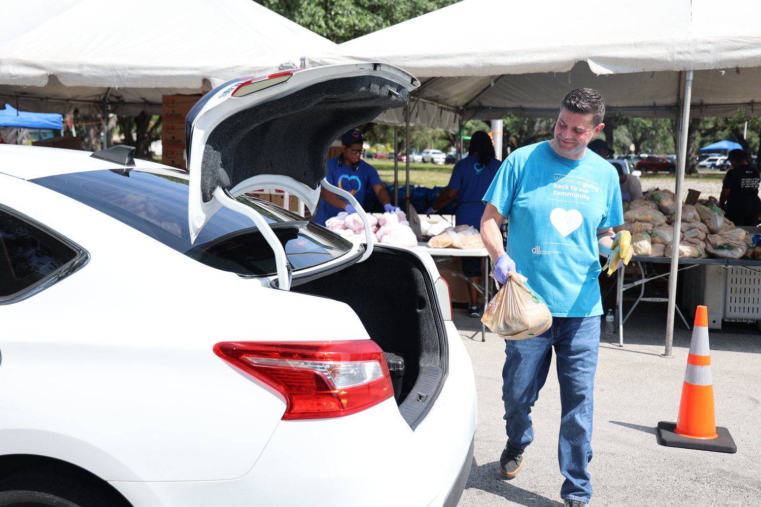 Volunteer carrying bags of food to a waiting car at a distribution