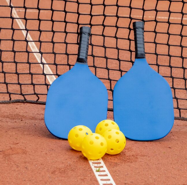 Two pickleball paddles and three balls on a court