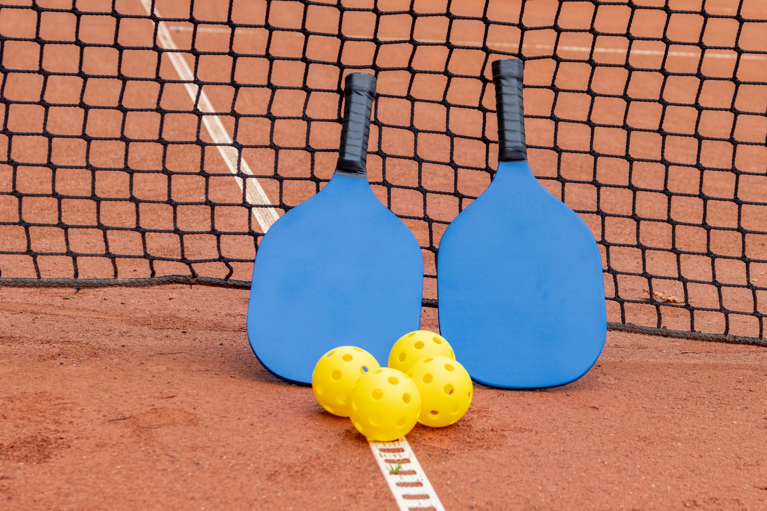 Two pickleball paddles and three balls on a court